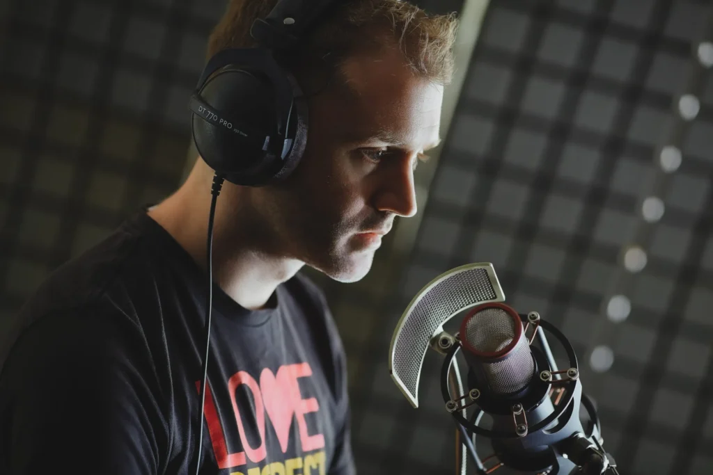 Focused male voice actor recording with Manley microphone and DT 770 headset.