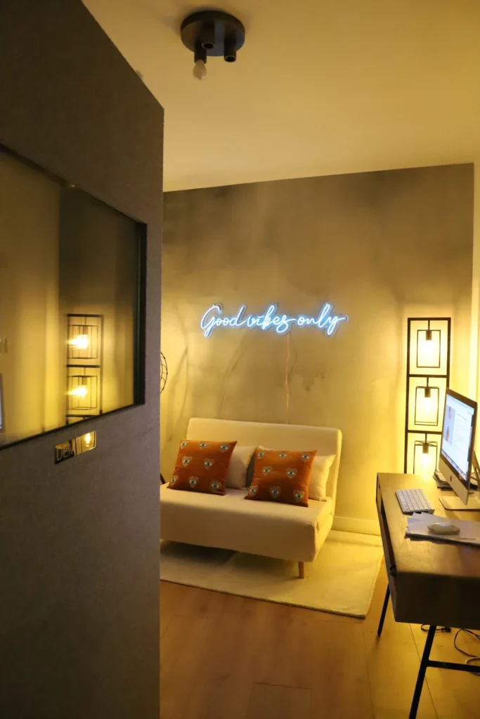 Warmly lit studio room with neon sign, sofa, and recording equipment setup.